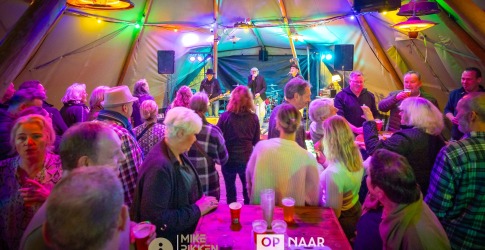 Mensen genieten van live muziek en drankjes in een kleurrijke tent tijdens een gezellig evenement.