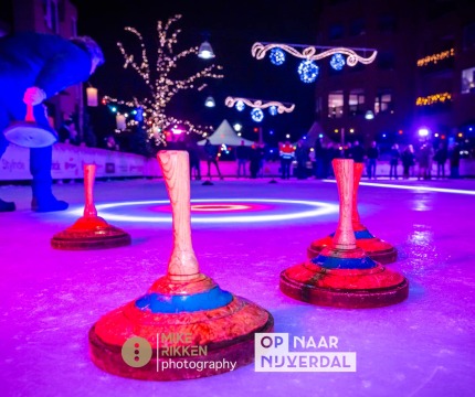 Verlicht ijsbaanscène met kegels en een persoon die curling speelt tijdens een avondwedstrijd.