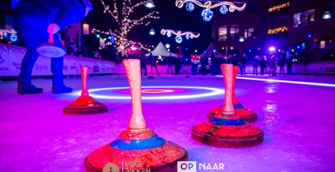 Verlicht ijsbaanscène met kegels en een persoon die curling speelt tijdens een avondwedstrijd.