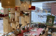 Kunststudio met hanglampen, kunstbenodigdheden, keramiek en schilderijen op een rode tafel.