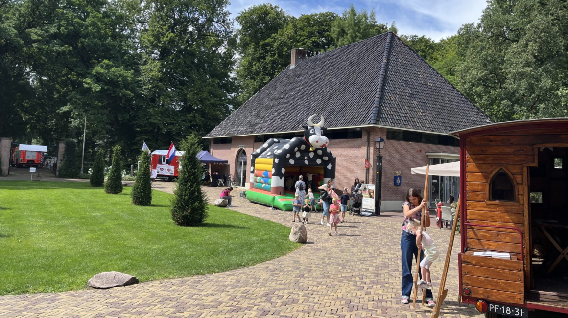 Kinderen spelen op een springkussen in de vorm van een koe bij een boerderijgebouw op een zonnige dag.