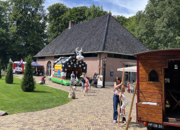 Kinderen spelen op een springkussen in de vorm van een koe bij een boerderijgebouw op een zonnige dag.