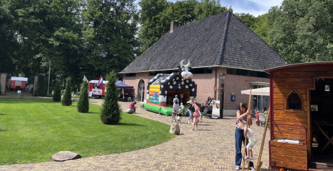 Kinderen spelen op een springkussen in de vorm van een koe bij een boerderijgebouw op een zonnige dag.