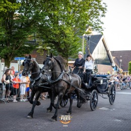 Twee zwarte paarden trekken een koets met twee personen tijdens een straatparade in Helderse Feest.