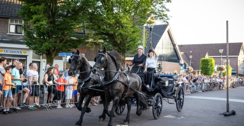 Twee zwarte paarden trekken een koets met twee personen tijdens een straatparade in Helderse Feest.