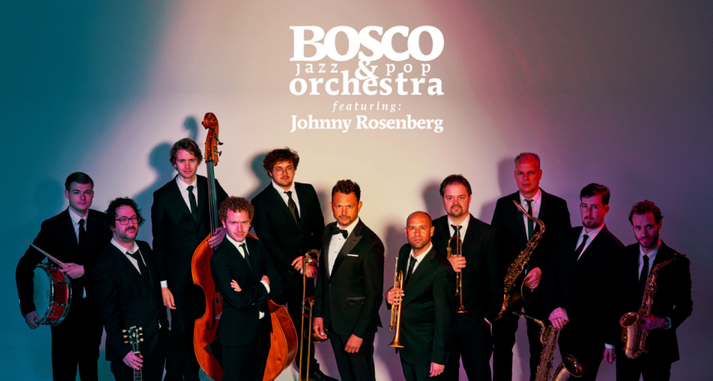 Groepsfoto van het BOSCO Jazz & Pop Orchestra met Johnny Rosenberg, allemaal in pakken met hun instrumenten.