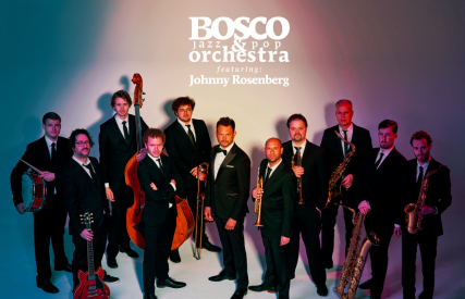 Groepsfoto van het BOSCO Jazz & Pop Orchestra met Johnny Rosenberg, allemaal in pakken met hun instrumenten.
